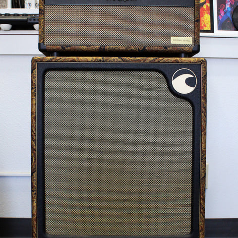 Full front view of a black amp head atop a matching cabinet, both with gold paisley trim and gold speaker grilles.