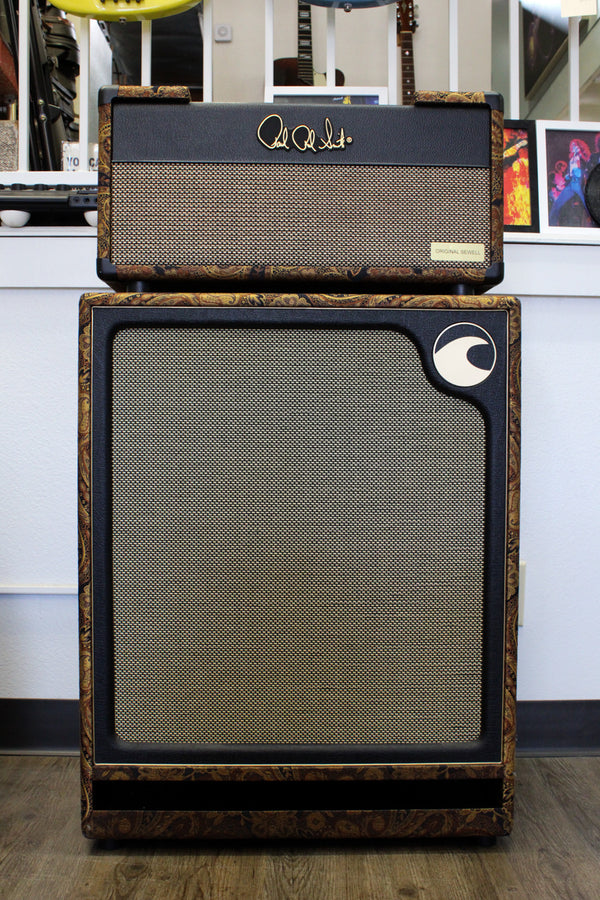 Full front view of a black amp head atop a matching cabinet, both with gold paisley trim and gold speaker grilles.