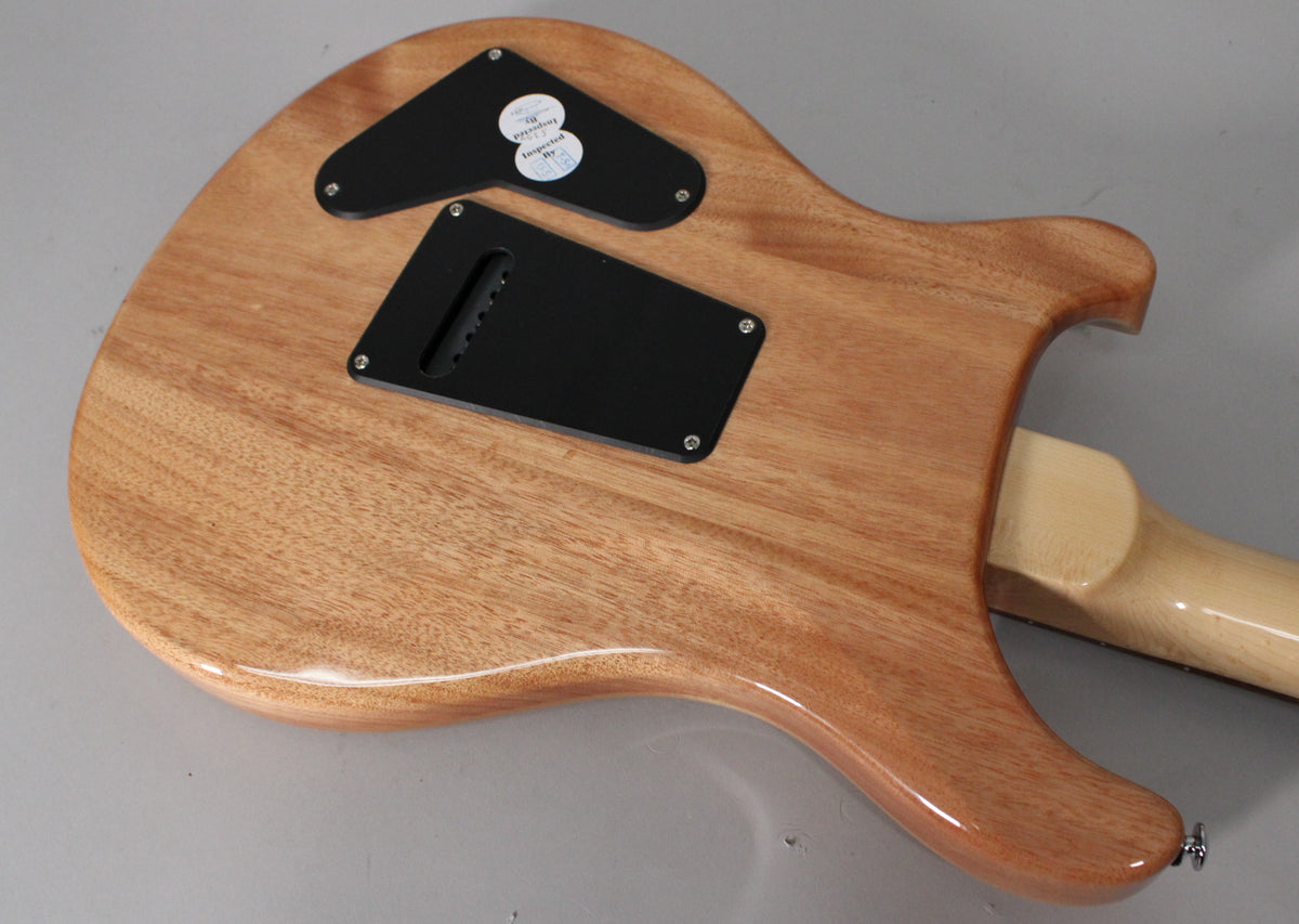 The guitar's back shows a glossy, light brown wood grain body with two black control cavity covers and a light maple neck.