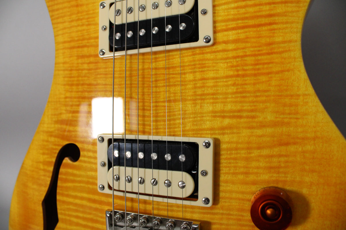 Close-up of the guitar's glossy, flamed yellow body, showing two cream-framed humbuckers, an f-hole, and a brown control knob.