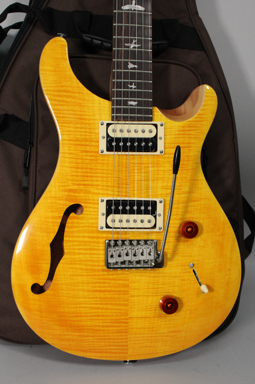 Close-up of a bright yellow semi-hollow electric guitar with a flamed maple top, f-hole, two humbuckers, and a tremolo bridge.