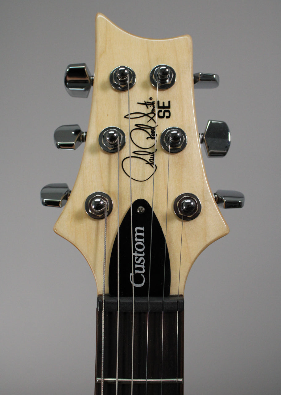 Close-up of the guitar's light wood headstock, showing six chrome tuners, a black truss rod cover, and the dark fretboard.