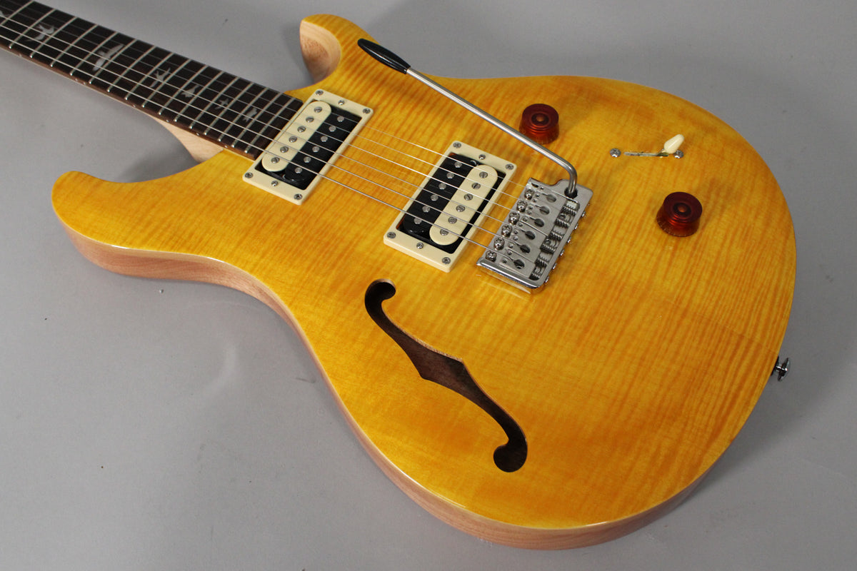 Angled view of a yellow flamed maple semi-hollow guitar with two cream humbuckers, a tremolo bar, and two dark red control knobs.