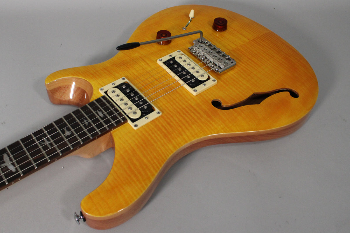 Overhead view of a yellow flamed-maple semi-hollow guitar with two cream humbuckers, a tremolo arm, and an f-hole.