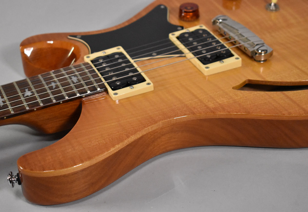 Close-up of the guitar's lower body, showing the sunburst finish, f-hole, two cream-colored humbucker pickups, and a chrome bridge.