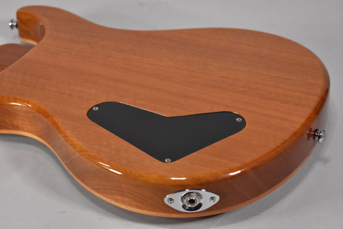 The guitar's glossy, light brown back shows a black electronics cover and a chrome output jack on the lower bout.