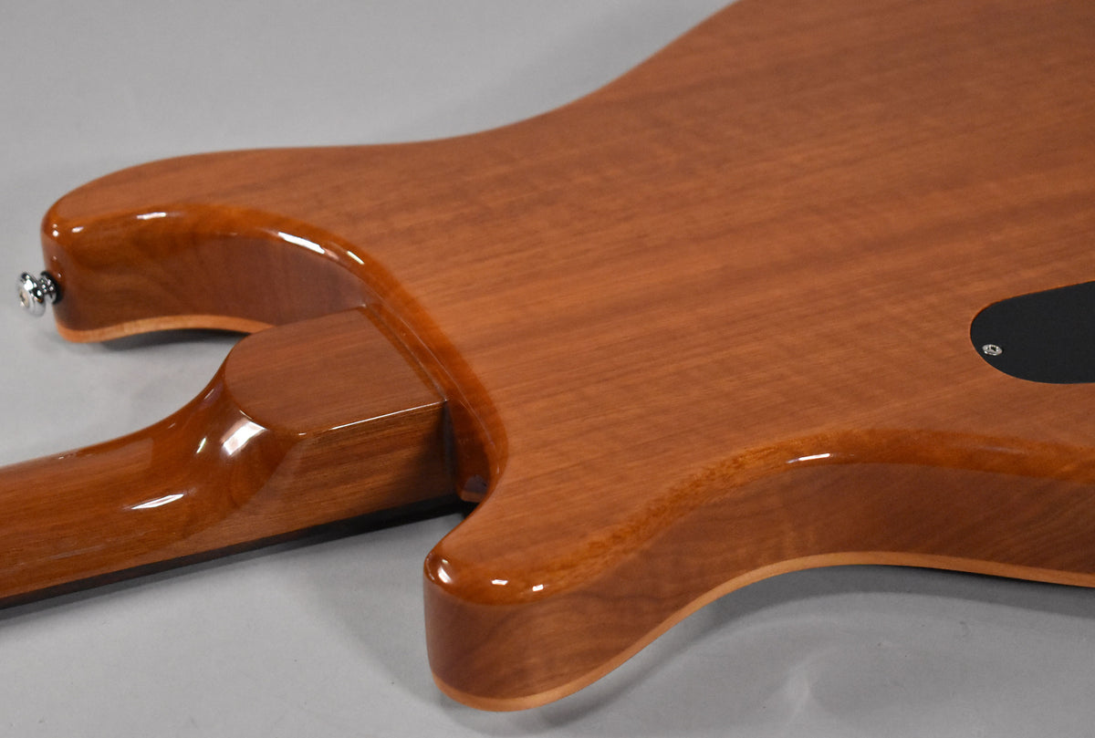 The guitar's glossy, reddish-brown back shows a set neck joint, lower horn, and a black control cavity cover near the bottom right.