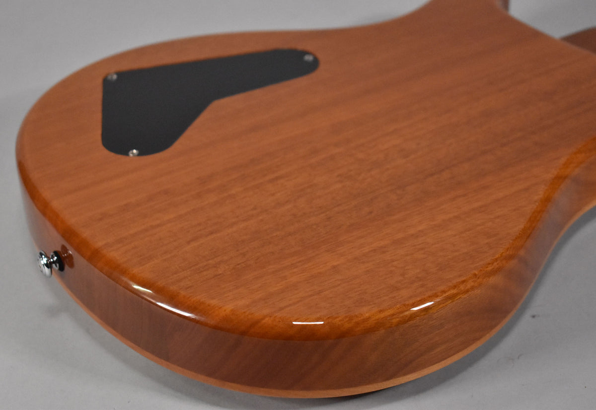 The back of a glossy, reddish-brown guitar body, showing a black control cavity cover and a chrome strap button on the lower bout.