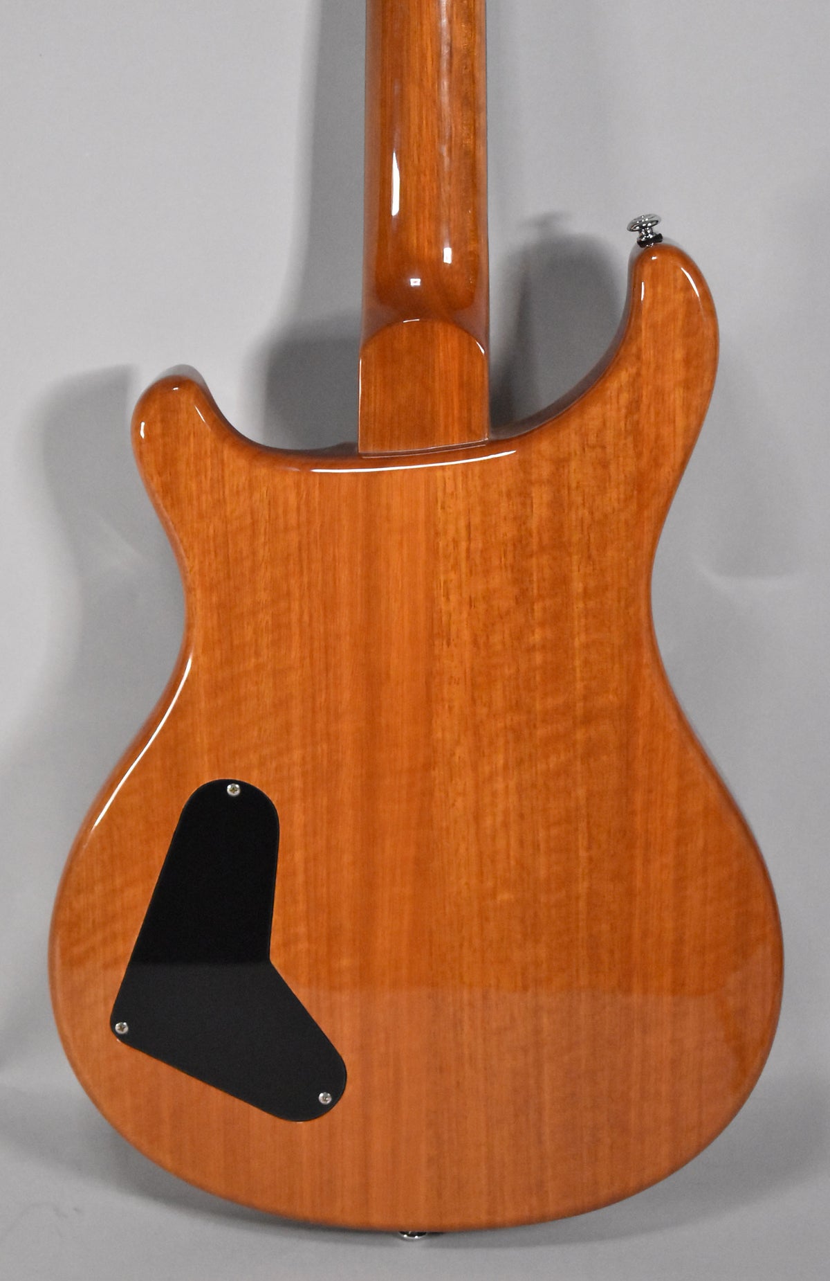 The guitar's glossy amber back and neck show subtle wood grain, with a black control cavity cover and a chrome strap button.