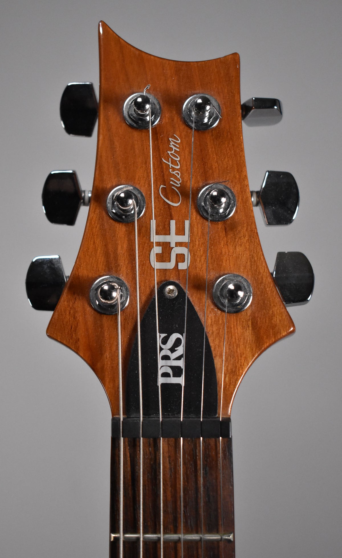Close-up of the guitar's headstock, showing the amber-finished wood, six chrome tuners, and the top of the dark fretboard.
