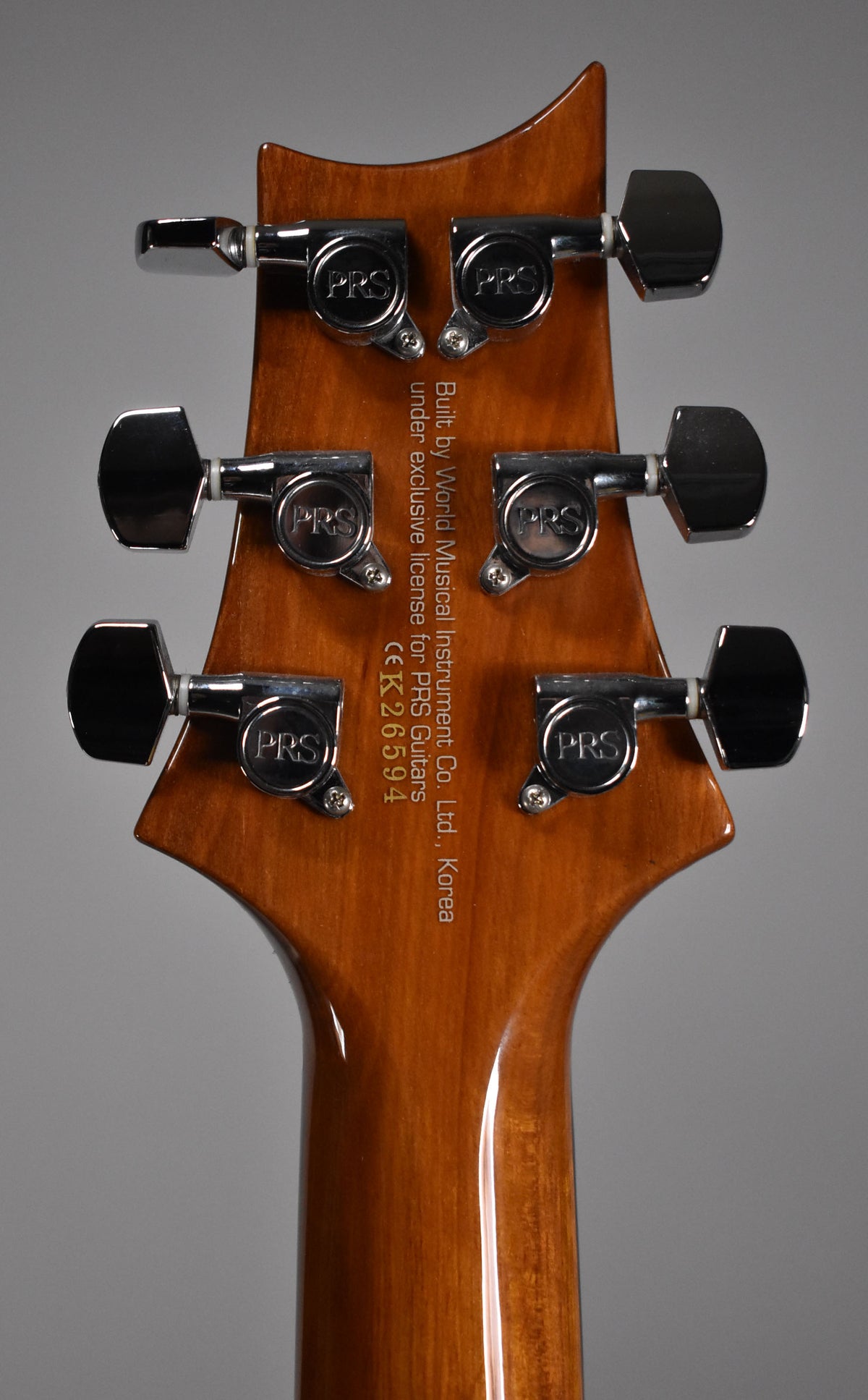 The back of a glossy, light brown guitar headstock with six chrome tuners, showing a faint scratch on the neck.