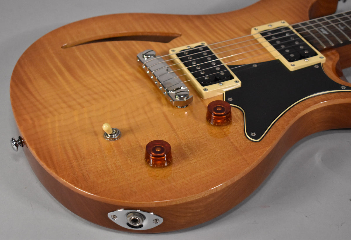 Close-up of the sunburst guitar body, showing the f-hole, two humbuckers with cream surrounds, black pickguard, and amber control knobs.