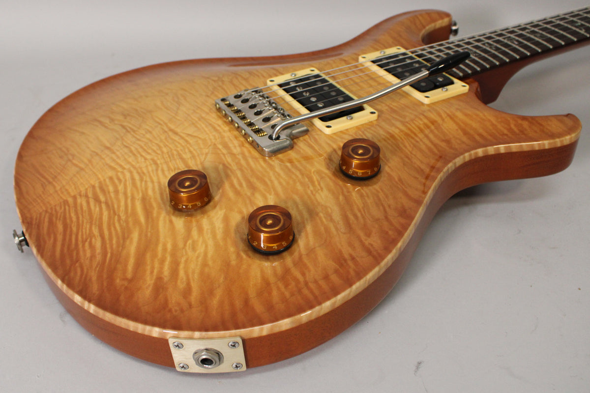 The guitar's sunburst flamed maple top, with three amber control knobs and a tremolo bridge, is angled from the lower bout.