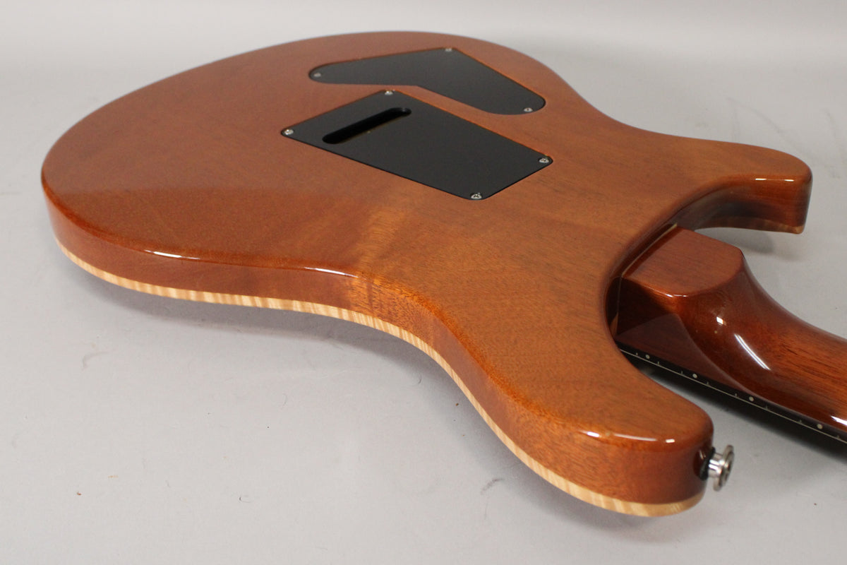 The guitar's sunburst back shows two black control cavity covers, a visible maple cap, and a chrome strap button.