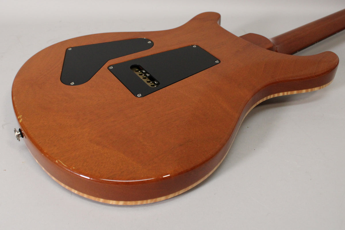 The guitar's sunburst back shows two black control plates, string-through ferrules, and light wear near the strap button.