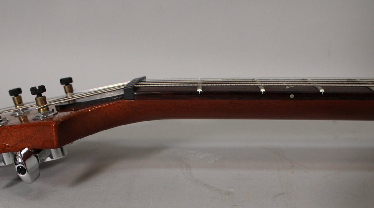 The guitar's headstock and upper neck are shown from the side, revealing a dark brown fretboard with white dot inlays.