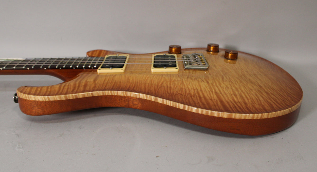 The guitar's sunburst top with flame maple grain is visible from the lower bout to the neck joint, showing cream pickups and amber knobs.