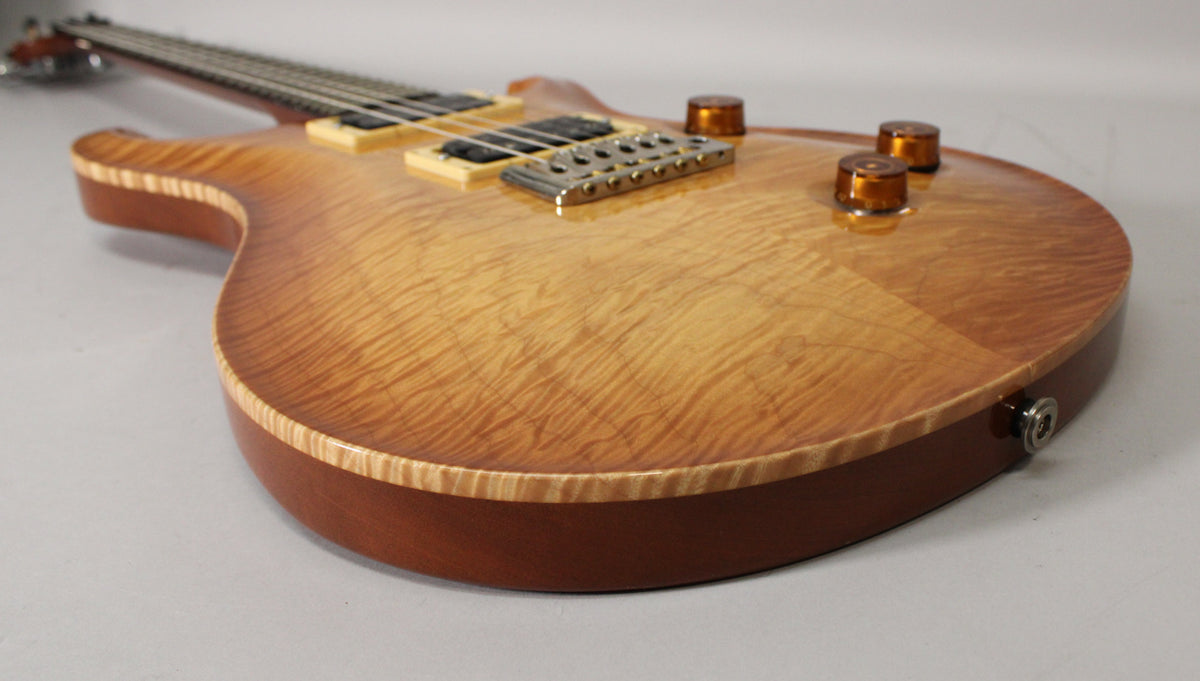 The guitar's sunburst flame maple top, with natural binding, is angled from the lower bout to the bridge and controls.