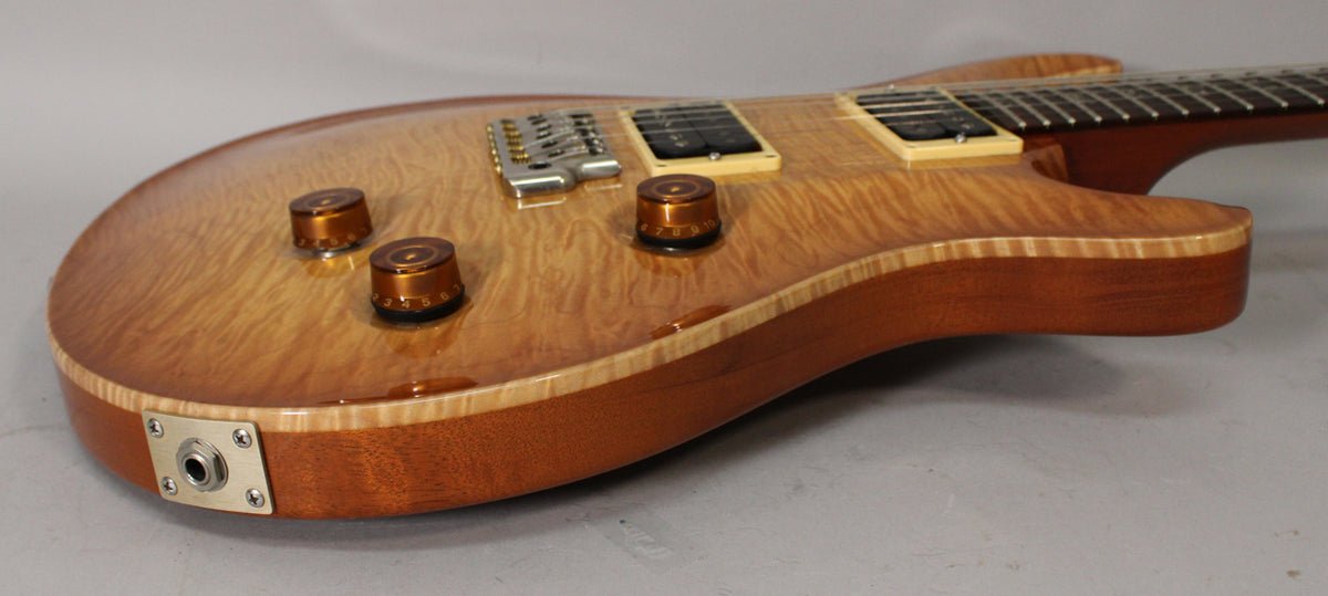The guitar's sunburst flame maple top, with three amber control knobs, is angled to show the output jack and lower bout.