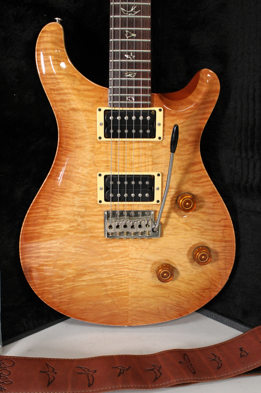 Close-up of a glossy sunburst electric guitar, showing the body, pickups with cream surrounds, tremolo arm, and three amber control knobs.