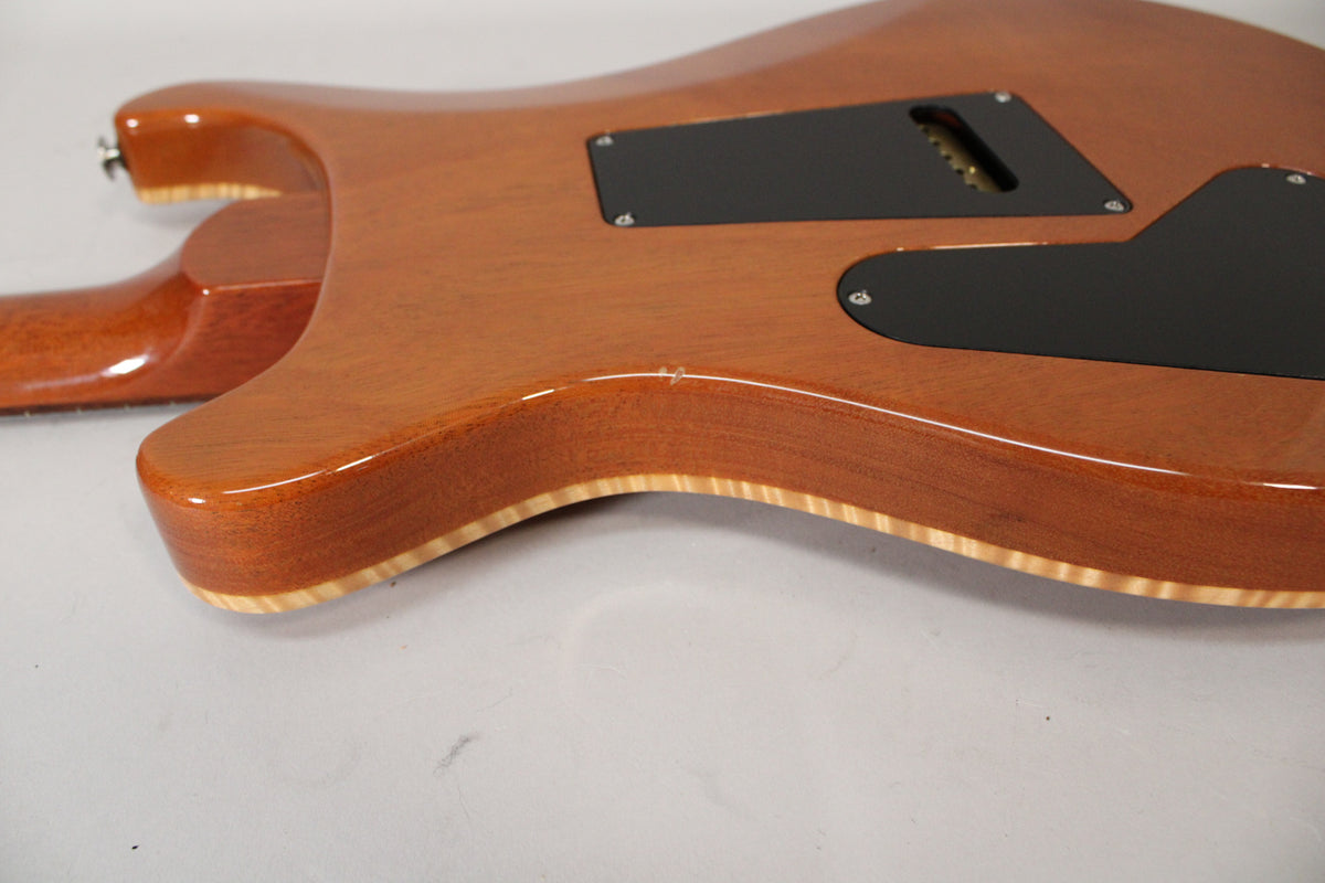 The guitar's sunburst back, showing the tremolo cavity cover, has a small ding on the upper bout and a visible flame maple binding.