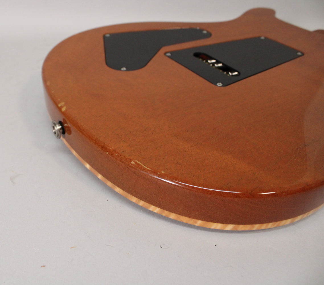 The guitar's sunburst back, showing two black control covers, a chrome output jack, and several chips along the bottom edge.