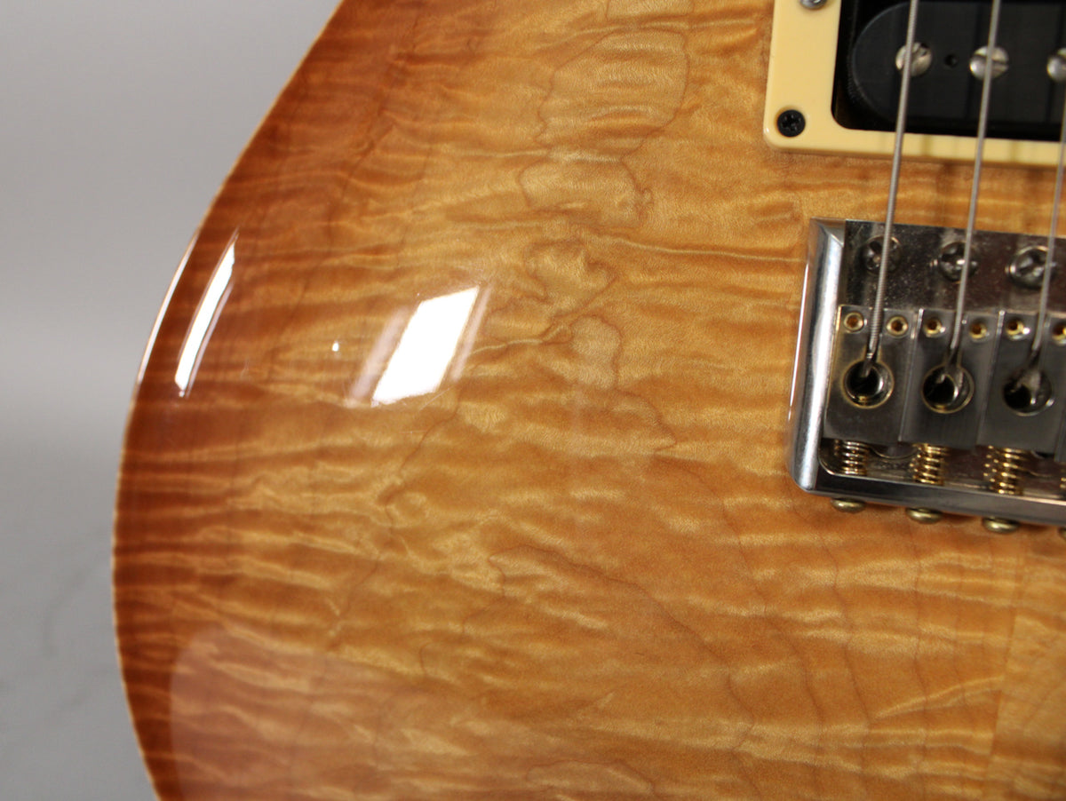 Close-up of the guitar's lower bout, showing the sunburst flame maple top, chrome bridge, and cream-ringed black humbucker.