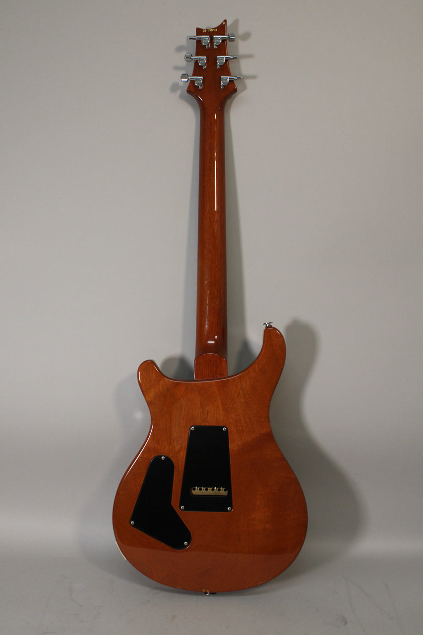The guitar's back is a glossy, reddish-brown, with two black control cavity covers and six chrome tuners on the headstock.