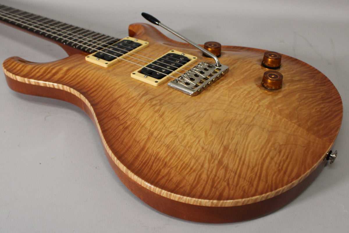 Close-up of a sunburst electric guitar, showing the flame maple top, cream humbucker pickups, chrome tremolo, and three amber knobs.