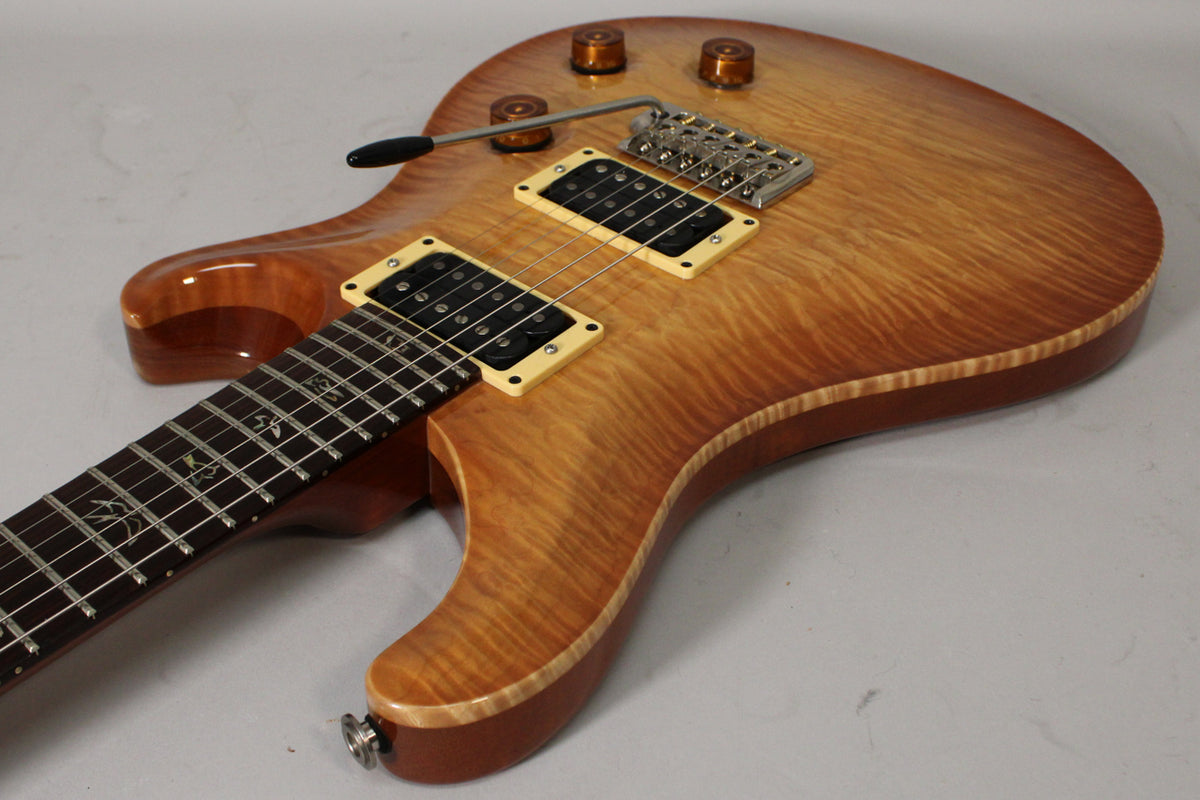 Angled view of a sunburst electric guitar with a flame maple top, cream pickup rings, a tremolo bridge, and bird inlays on the fretboard.