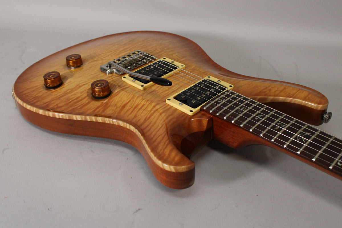 The sunburst electric guitar's body, with a flame maple top and cream binding, is angled to show the bridge, pickups, and controls.