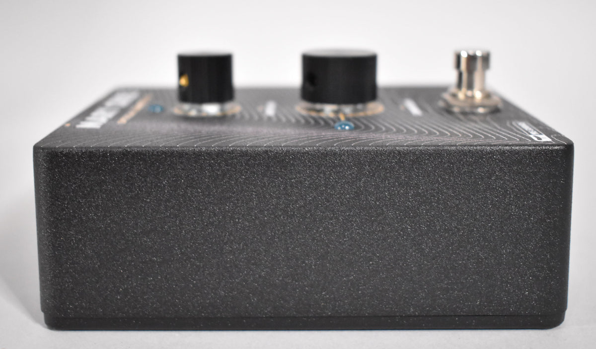 The dark gray textured pedal is viewed from the right side, showing two black knobs and a silver footswitch on the top surface.
