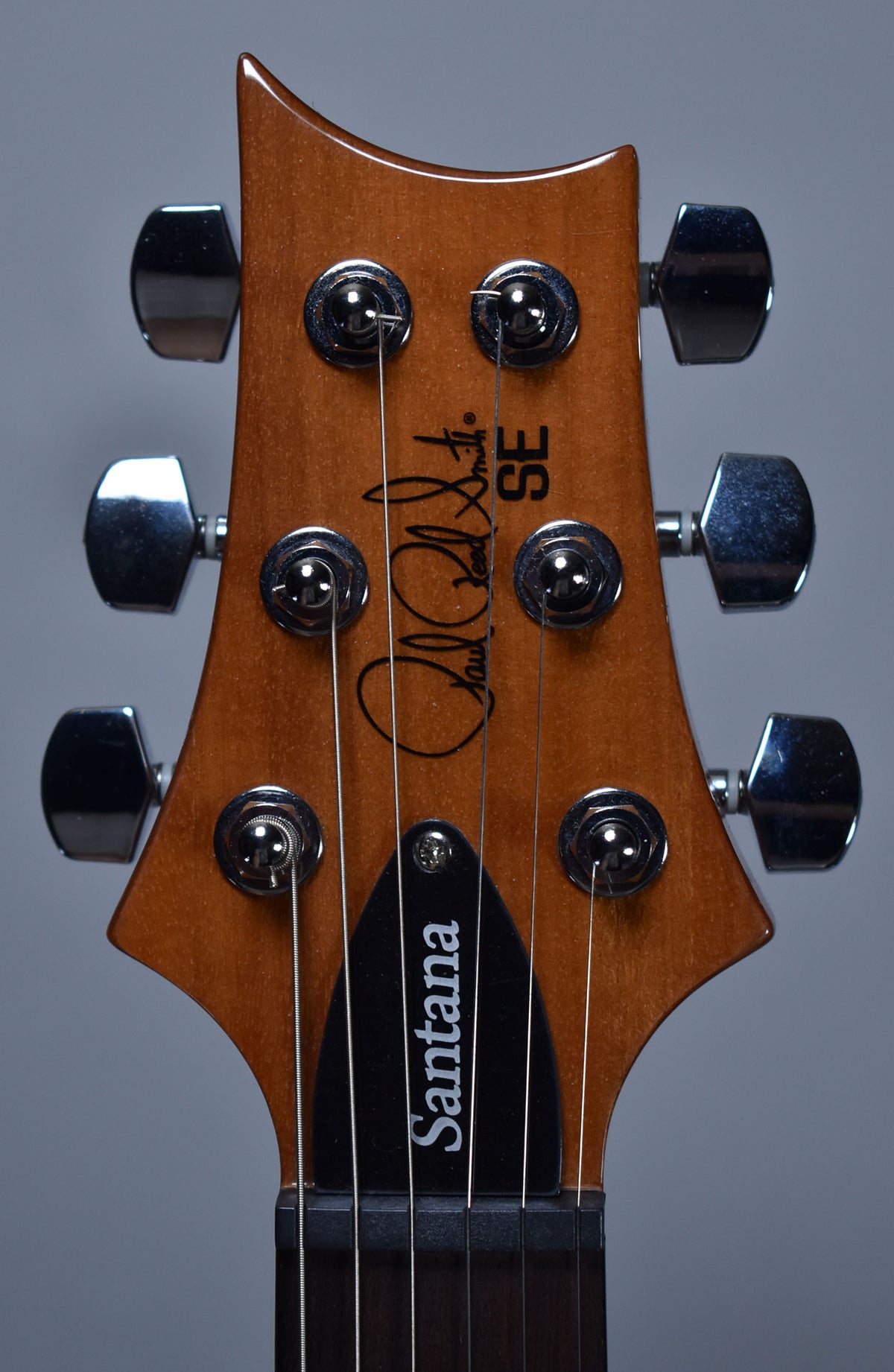 Close-up of the guitar's headstock, showing a glossy brown finish, six chrome tuners, and a black truss rod cover.