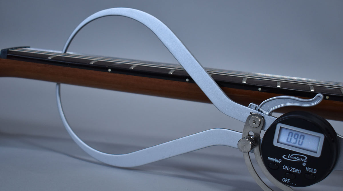 The guitar's dark brown neck and fretboard are measured by a silver digital caliper displaying "0.90".