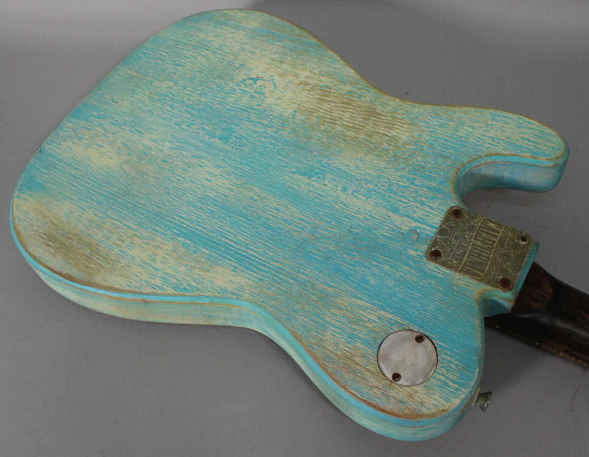 The back of a blue relic guitar body, heavily worn to reveal pale wood, with a metal neck plate and circular control cover.