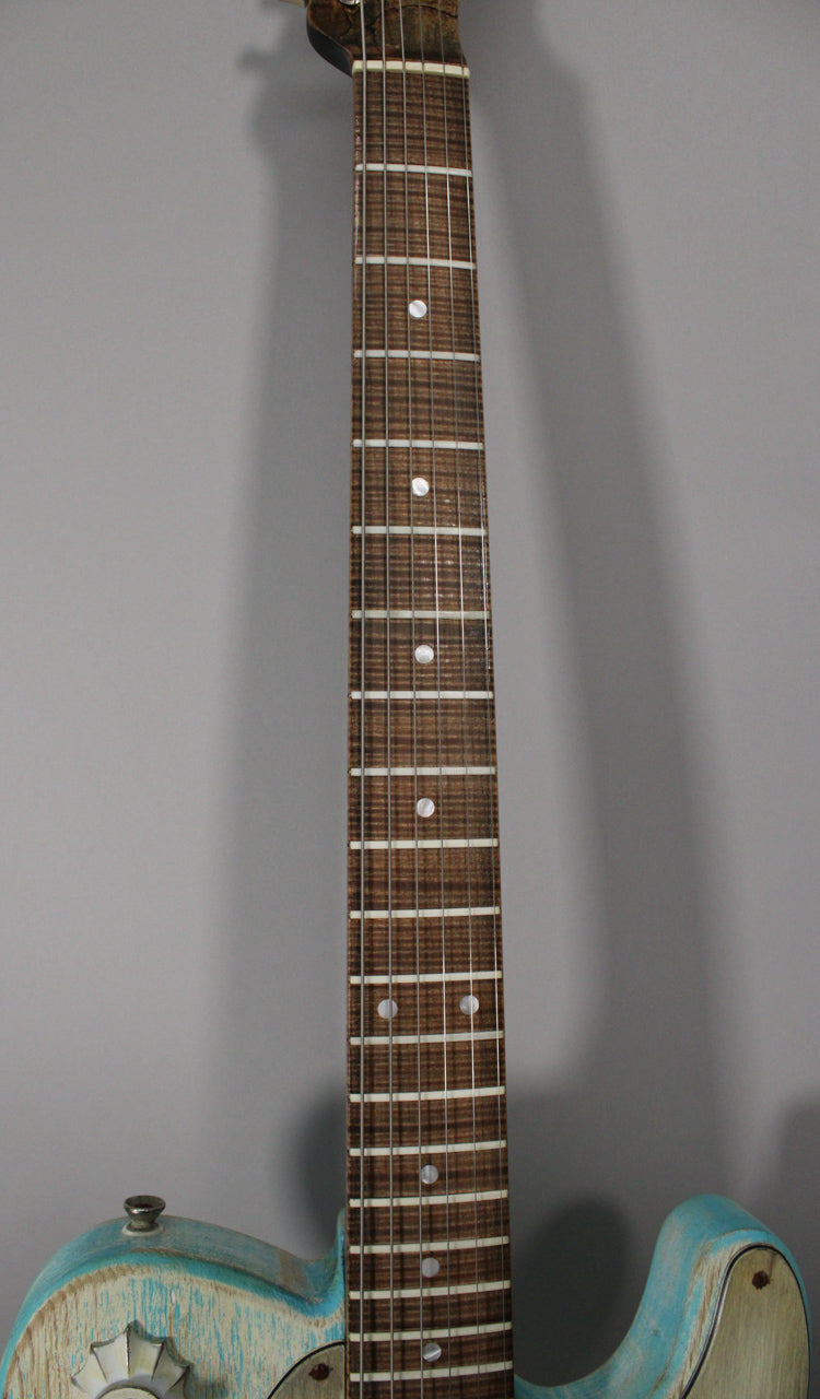 The guitar's neck and upper body are visible, showing a dark wood fretboard with white dot inlays and a heavily relic'd blue finish.