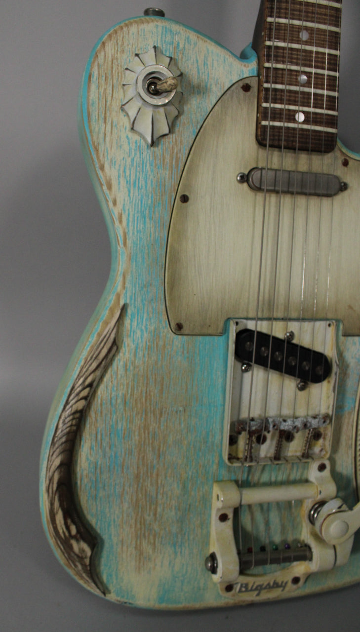 Close-up of the guitar body, showing the heavily relic'd blue-green finish, cream pickguard, Bigsby tremolo, and a decorative switch.