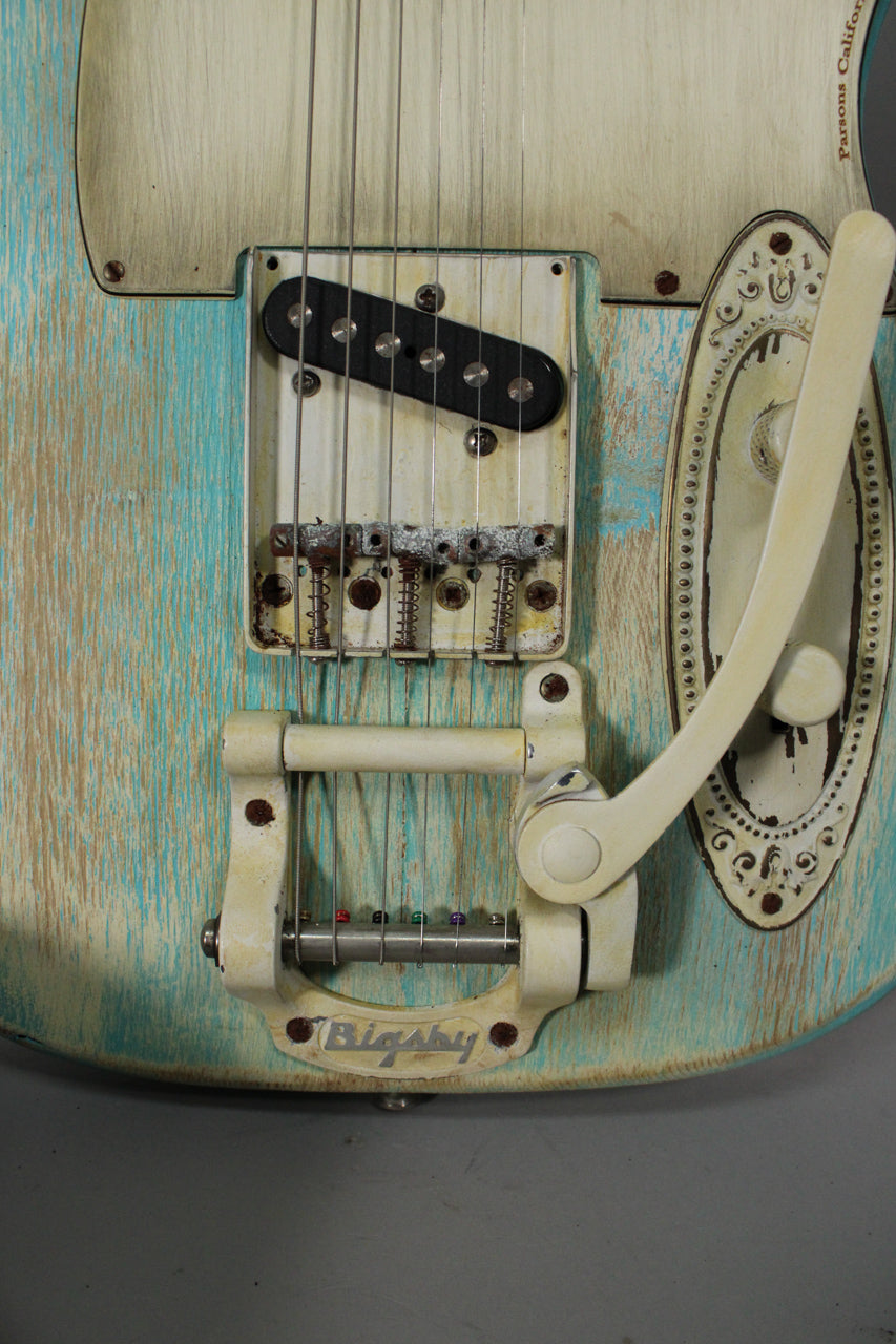 Close-up of the guitar's lower body, showing a heavily relic'd blue and cream finish, a rusty bridge, black single-coil pickup, and a cream Bigsby tremolo.