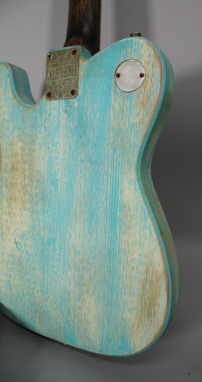 The back of a light blue guitar body with heavy relic wear, showing a metal neck plate and a round metal control cover.