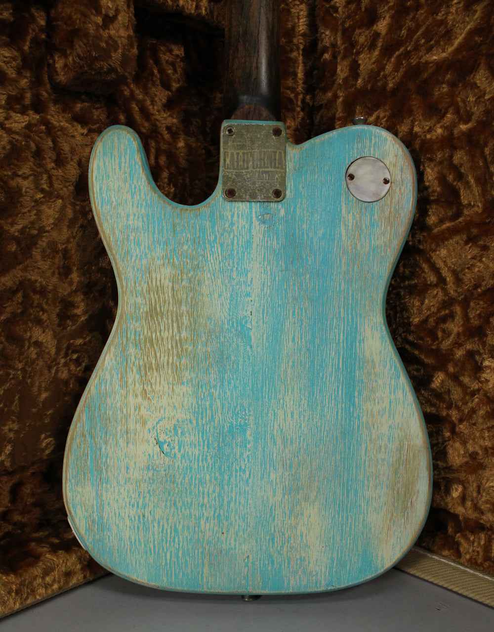 Full back view of the electric guitar, showing its heavily relic'd blue finish with significant wear, a metal neck plate, and a circular control cover.