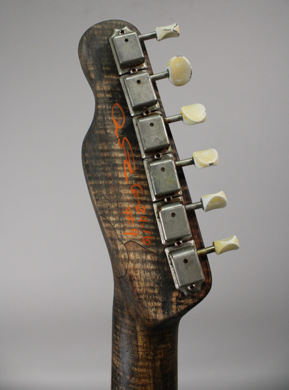 Close-up of the guitar's dark, heavily relic'd headstock with orange lettering, showing six aged metal tuners with chipped cream buttons.