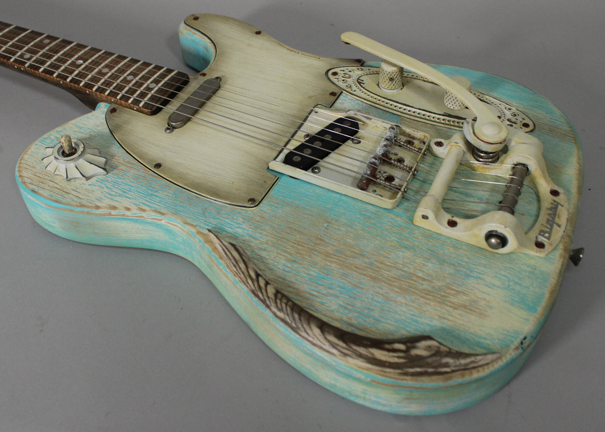 Close-up of the guitar's body, showing a heavily relic'd blue finish with exposed wood grain, cream pickguard, and Bigsby tremolo.
