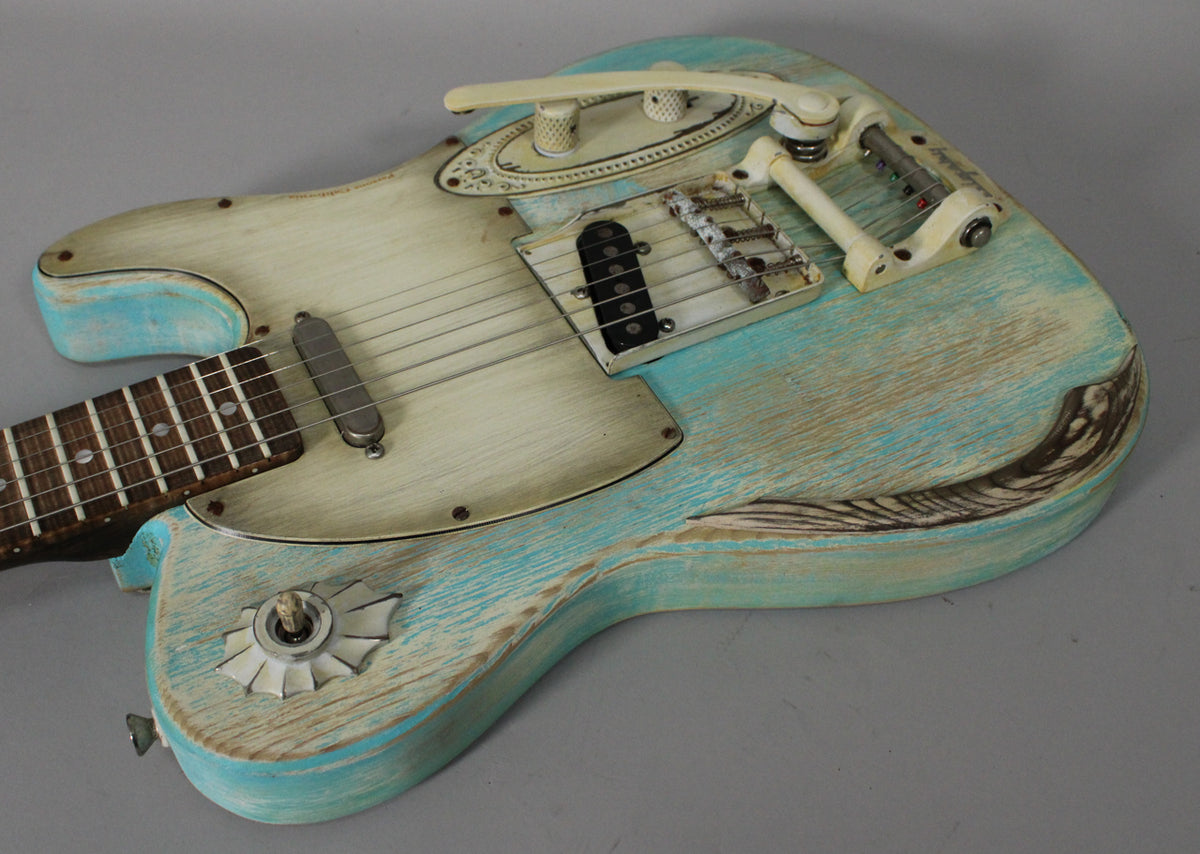 Close-up of a heavily relic'd teal and cream electric guitar with a Bigsby-style tremolo, two pickups, and unique decorative controls.