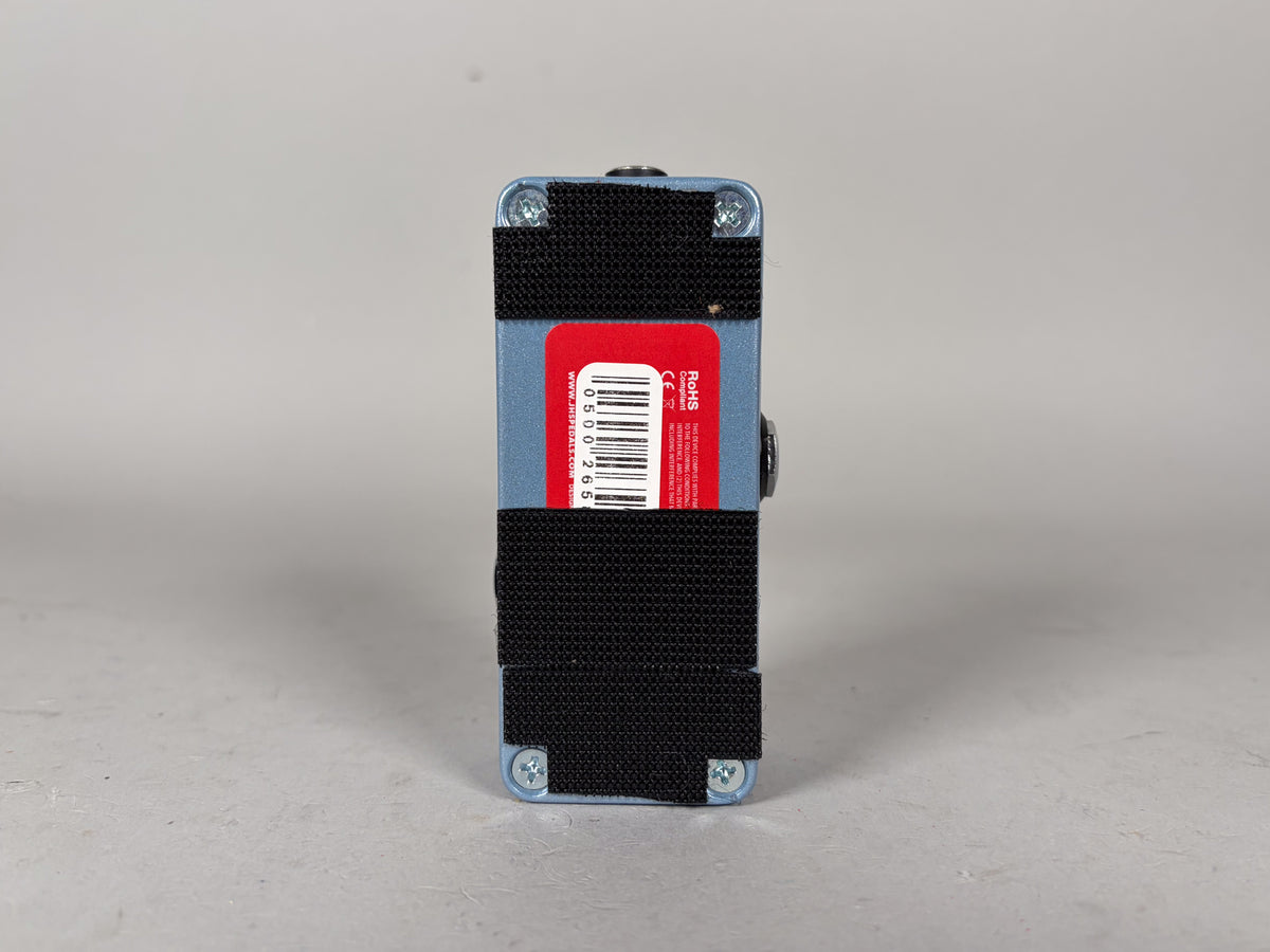 The light blue pedal is viewed from the side, with black hook-and-loop strips and a red sticker on its base.