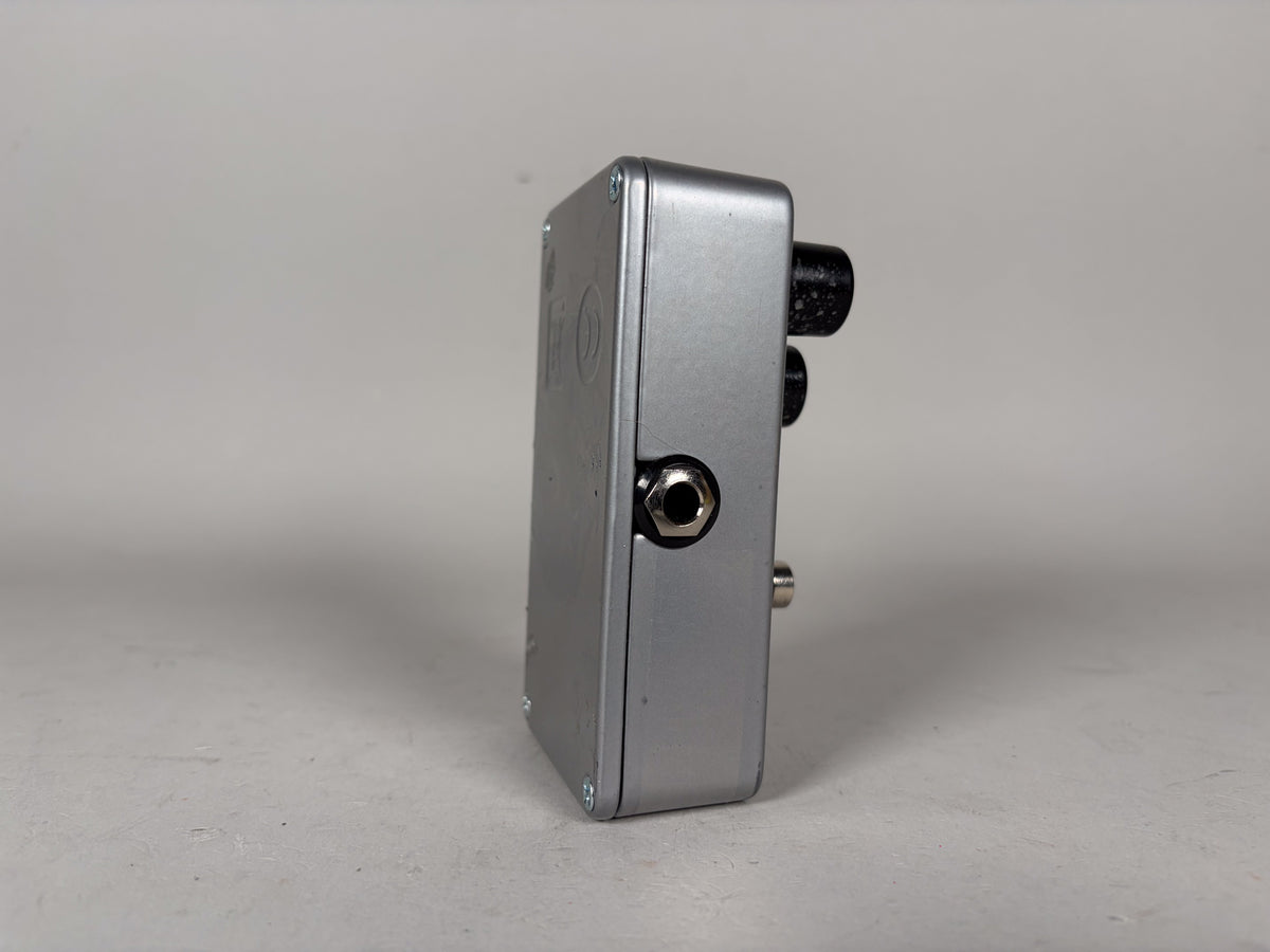 Side view of a silver Electro-Harmonix Big Muff Rams Head Reissue Fuzz Pedal, showing an input jack and two black knobs.
