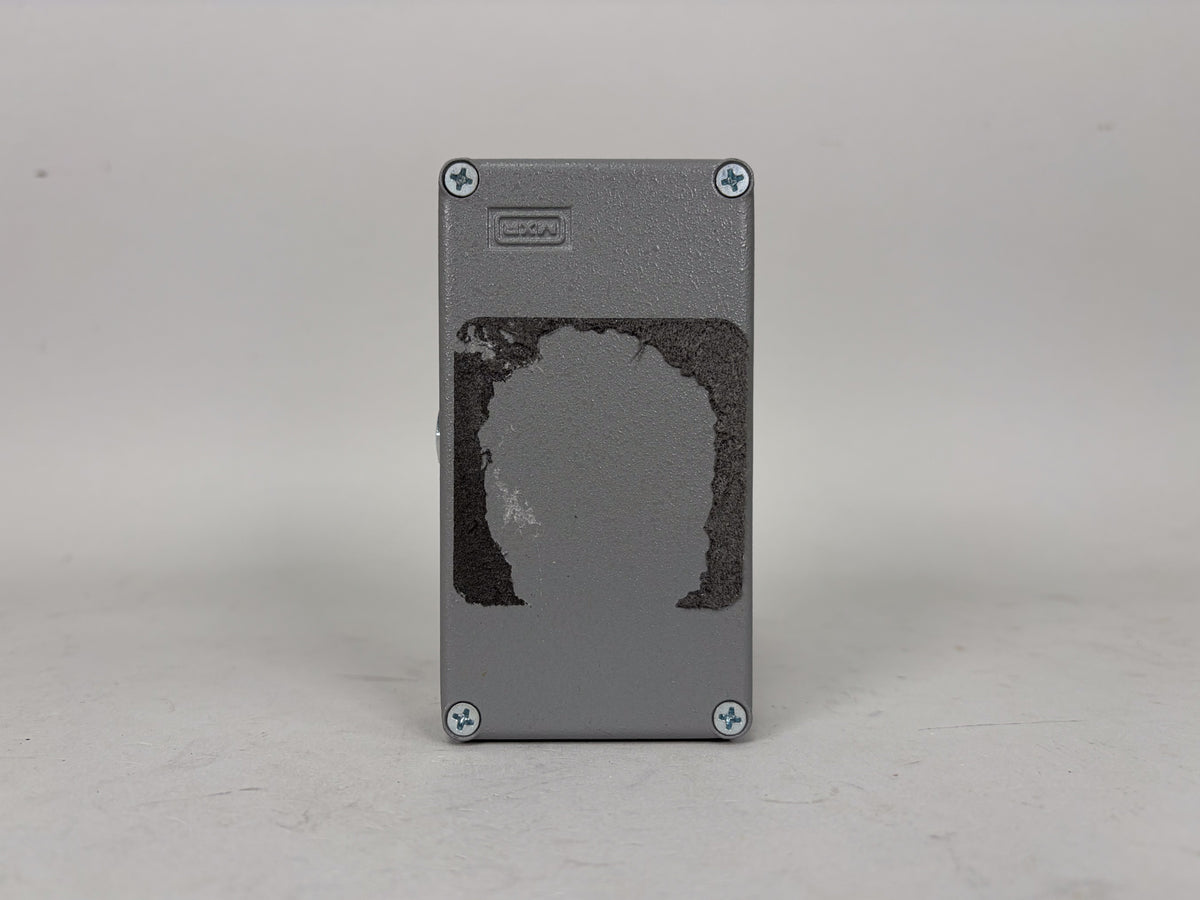 The gray pedal is viewed from the back, showing four silver Phillips head screws and a large, dark, irregular patch of residue.