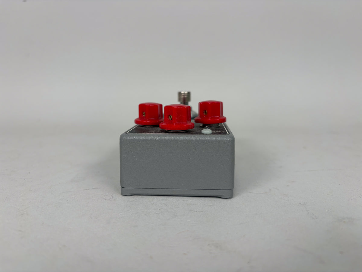 The gray effect pedal is viewed from the right side, showing three red control knobs and a silver footswitch on its top surface.