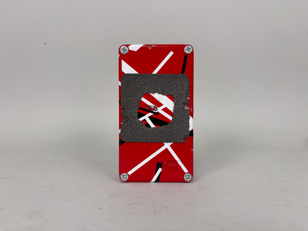 The pedal's red, white, and black striped bottom is visible, with a worn, rectangular grey velcro pad adhered to the center.