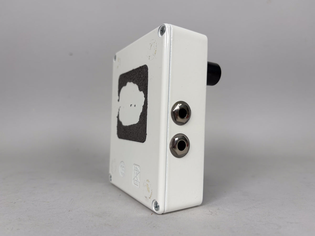 A white guitar pedal, viewed from the right side, showing two input jacks and a black control knob on the top right.
