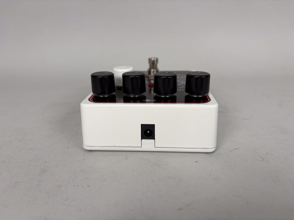 The white pedal is viewed from the rear, showing the DC power input jack and four black control knobs on top.